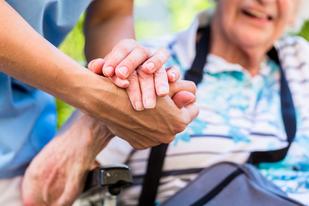 nursing home nurse holding hand of elderly woman